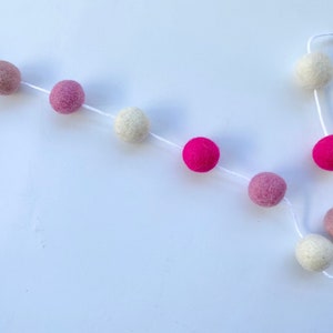 May include: A garland of felt balls in pink, white, and beige colors strung on white twine.