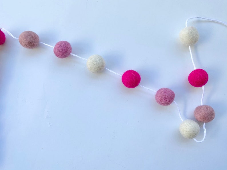 May include: A garland of felt balls in pink, white, and beige colors strung on white twine.
