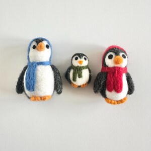 May include: Three felt penguin ornaments, one with a blue scarf, one with a red scarf, and one with a green scarf.