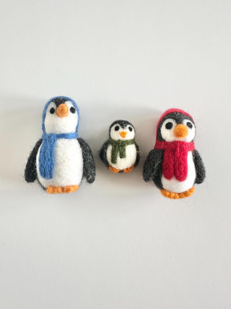 May include: Three felt penguin ornaments, one with a blue scarf, one with a red scarf, and one with a green scarf.