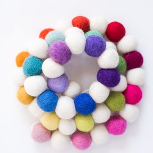 May include: A colorful garland made of felt balls in various shades of blue, green, yellow, orange, red, pink, and purple. The garland is strung together with white felt balls.