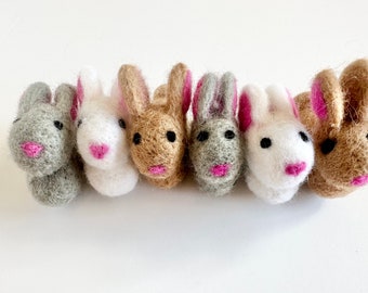 May include: Six felt bunny rabbit figurines in a row. The bunnies are in different colors: gray, white, brown, gray, white, and brown. Each bunny has pink felt ears and a pink felt nose.