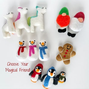 May include: A collection of felt ornaments, including a gingerbread person, snowmen, penguins, gnomes, and unicorns. The ornaments are all white with colorful details. The text "Choose Your Magical Friend!" is written in red on a white background.