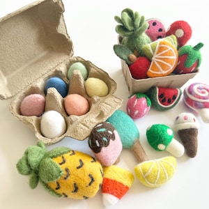 May include: A collection of colorful felt food items, including a pineapple, watermelon slices, strawberries, and a variety of other fruits and sweets. An egg carton holds felt eggs in pastel colors. A small cardboard container holds more felt fruits.