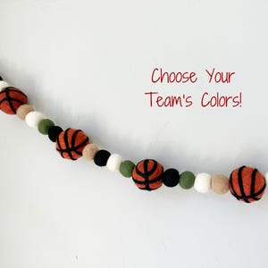 May include: A felt ball garland featuring basketballs and solid-colored balls in various hues. The basketballs are orange with black lines. The text "Choose Your Team's Colors!" is written in red.