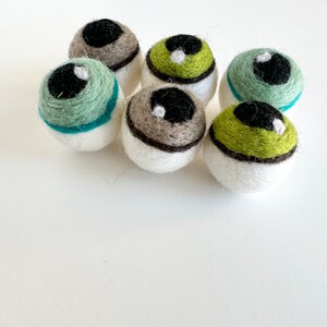 May include: Six felt eyeball ornaments in various colors, including green, brown, and white. The eyeballs have black pupils and white highlights.