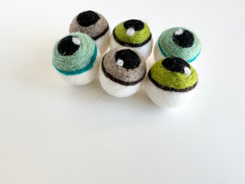 May include: Six felt eyeball ornaments in various colors, including green, brown, and white. The eyeballs have black pupils and white highlights.
