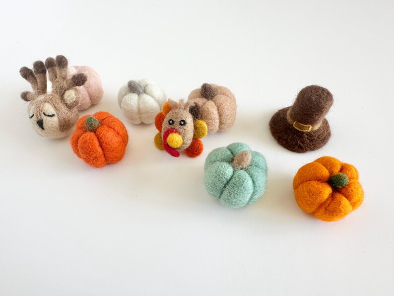 May include: A collection of felt crafts for Thanksgiving, including a sleeping deer, a turkey, a pilgrim hat, and pumpkins in various colors.