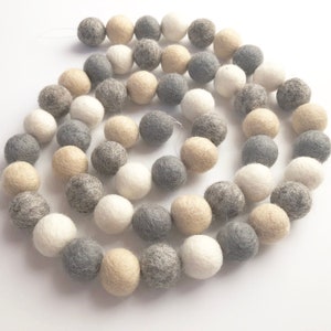 May include: A garland of felt balls in white, gray, and beige colors. The balls are strung together on a white thread.