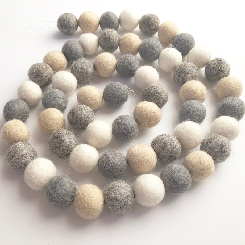 May include: A garland of felt balls in white, gray, and beige colors. The balls are strung together on a white thread.