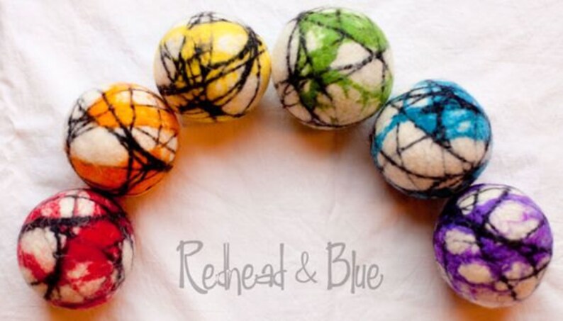 May include: Seven colorful felt balls arranged in an arc. Each ball is a different color, including red, orange, yellow, green, blue, and purple, with a white base and black web-like design. The text "Redhead & Blue" is at the bottom.