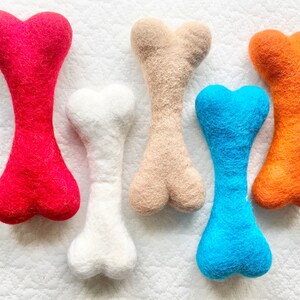 May include: Five felt dog chew toys in different colors: red, white, beige, blue, and orange. The toys are shaped like bones.
