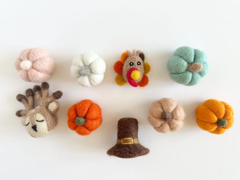 May include: A collection of felt ornaments for Thanksgiving, including a turkey, pumpkins, a deer, a pilgrim hat, and a white pumpkin.