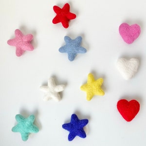 May include: A set of felt stars and hearts in various colors, including red, pink, blue, yellow, white, and green. The felt shapes are arranged in a circle on a white background.