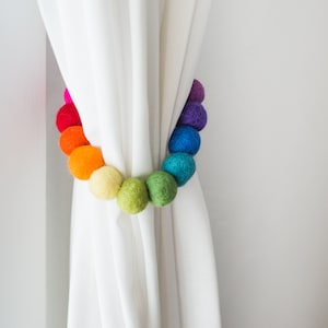 May include: A rainbow colored felt ball curtain tieback. The balls are strung together in a circle and are used to hold back curtains.