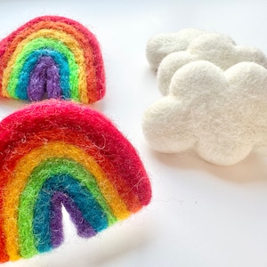 May include: Two felt rainbows, one red, orange, yellow, green, blue, indigo, and violet, and the other a similar colour scheme but with a lighter red, orange, and yellow.  The rainbows are handmade and have a fuzzy texture.  There are three white felt clouds in the background.