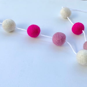 May include: A garland of felt balls in white, pink, and hot pink colors strung together with white string.