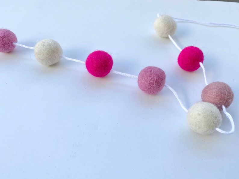 May include: A garland of felt balls in white, pink, and hot pink colors strung together with white string.