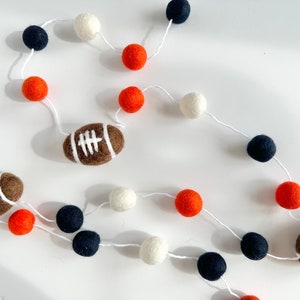 Puede incluir: Una guirnalda con bolas de fieltro blancas, naranjas y negras y dos balones de f&uacute;tbol de fieltro marrones.