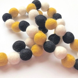 May include: A garland of felt balls in black, white, and yellow. The balls are strung together on a white string.
