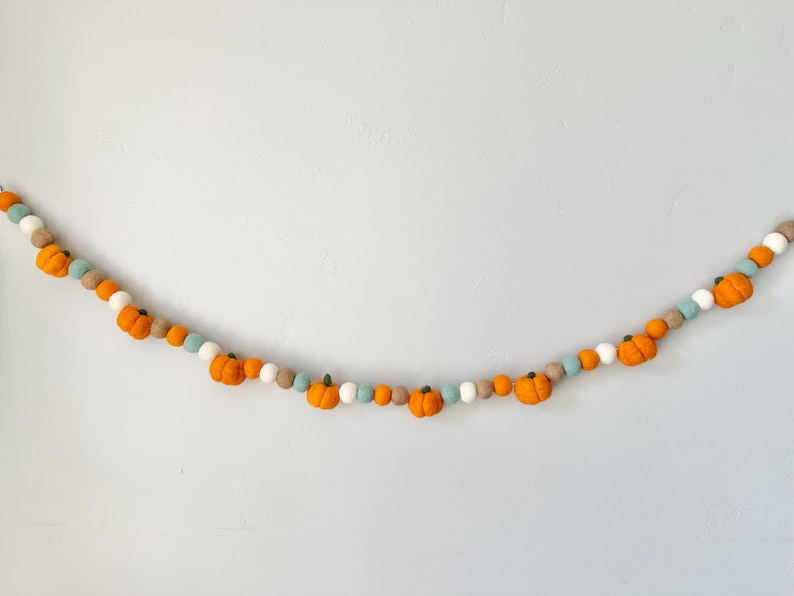 May include: A garland of felt pumpkins in orange, white, and light blue. The garland is strung together with a white string.
