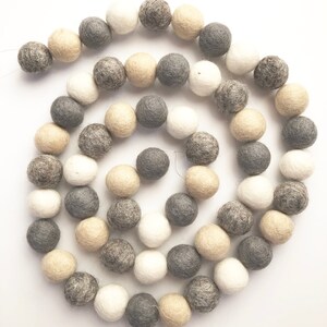 May include: A garland of felt balls in shades of gray, beige, and white. The balls are strung together on a white background.