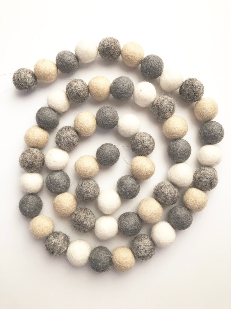 May include: A garland of felt balls in shades of gray, beige, and white. The balls are strung together on a white background.