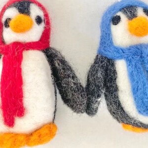 May include: Two felt penguin ornaments, one with a red scarf and hat, the other with a blue scarf and hat.
