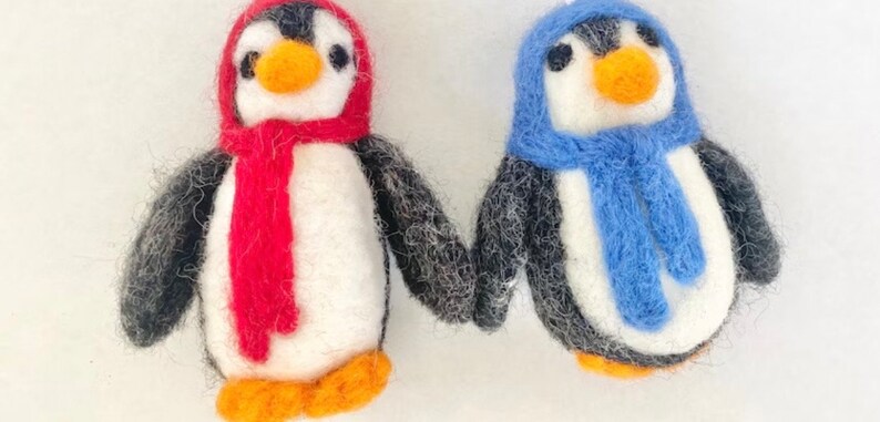 May include: Two felt penguin ornaments, one with a red scarf and hat, the other with a blue scarf and hat.