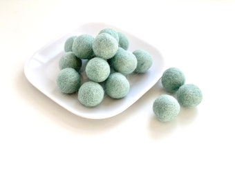 May include: A white plate with a pile of light green felt balls. There are three more light green felt balls on the white surface next to the plate.
