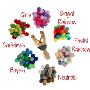 May include: A wooden slingshot is surrounded by colorful felt balls in various color palettes: Girly, Christmas, Boyish, Bright Rainbow, Pastel Rainbow, and Neutrals. Text labels identify each color grouping.