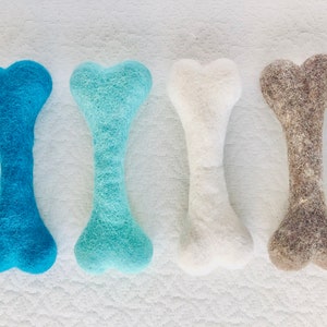May include: Four felt dog chew toys in the shape of bones. The bones are in shades of blue, white, and brown.