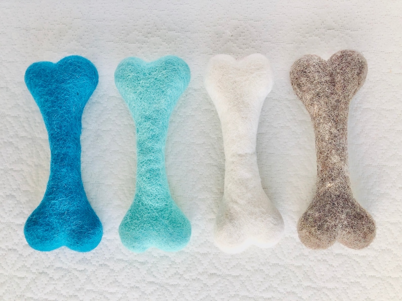 May include: Four felt dog chew toys in the shape of bones. The bones are in shades of blue, white, and brown.