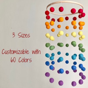 May include: A rainbow felt ball mobile with a wooden ring. The mobile has 3 sizes of felt balls in a rainbow color pattern. The text "3 Sizes Customizable with 60 Colors" is visible in the image.