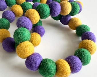 May include: A garland of felt balls in purple, green, and yellow. The balls are strung together to create a festive decoration.