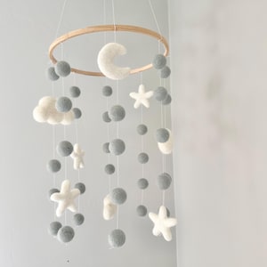 May include: A gray and white felt baby mobile with a wooden ring, a crescent moon, stars, and clouds. The mobile is hanging from the ceiling.