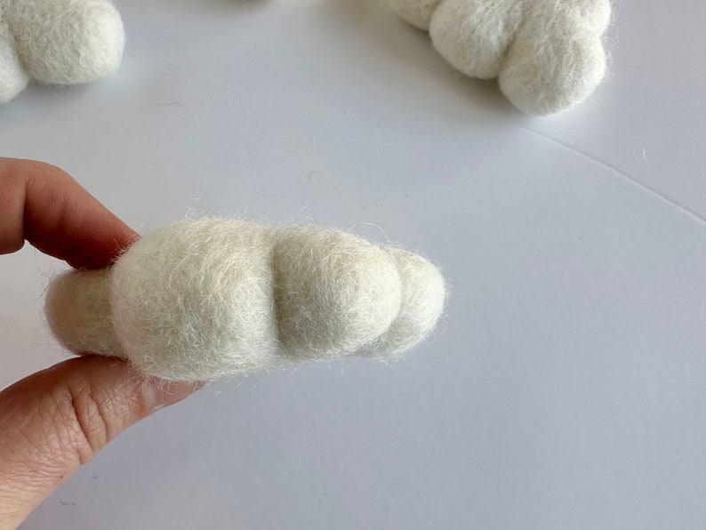 May include: A white felt cloud ornament with a rounded shape and a textured surface.