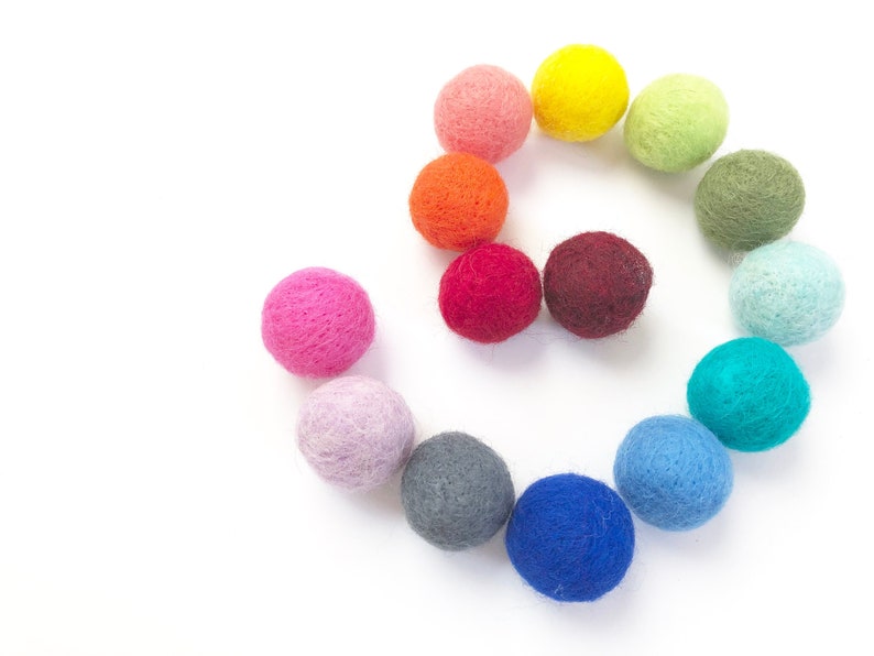 May include: A rainbow of colors in a spiral pattern of felt balls. The balls are arranged in a circle with the colors transitioning from pink to red, orange, yellow, green, blue, and purple.