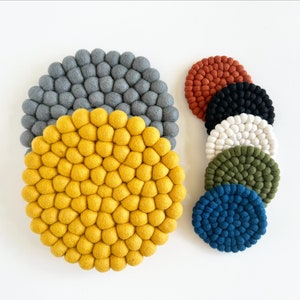 May include: Set of 7 round felt coasters in various colors, including gray, yellow, orange, black, white, green, and blue. The coasters are made of small felt balls.
