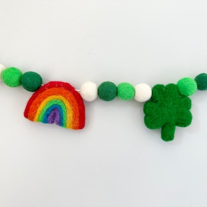 May include: A felt garland with green and white pom poms, a rainbow, and a shamrock.
