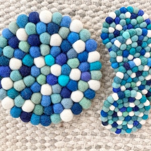 May include: Two round felt coasters in shades of blue, white, and green. The larger coaster is circular, while the smaller coaster is shaped like a teardrop.