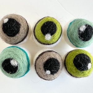 May include: Six felt eye balls in various colors, including green, brown, and blue. Each eye ball has a black pupil and a white highlight.