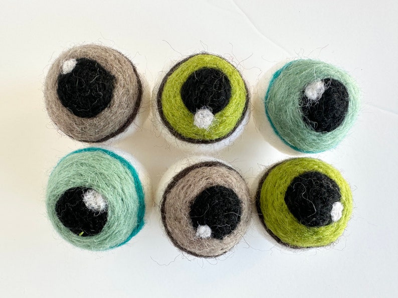 May include: Six felt eye balls in various colors, including green, brown, and blue. Each eye ball has a black pupil and a white highlight.