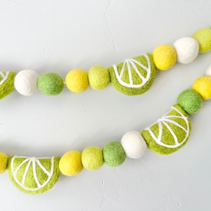 May include: A lime green and yellow felt garland with lime slices. The garland is made of felt balls and lime slices with white stitching.