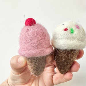 Pode incluir: Dois cones de gelado de feltro. Um &eacute; rosa com uma cereja vermelha no topo. O outro &eacute; branco com granulado colorido. Ambos t&ecirc;m cones castanhos.
