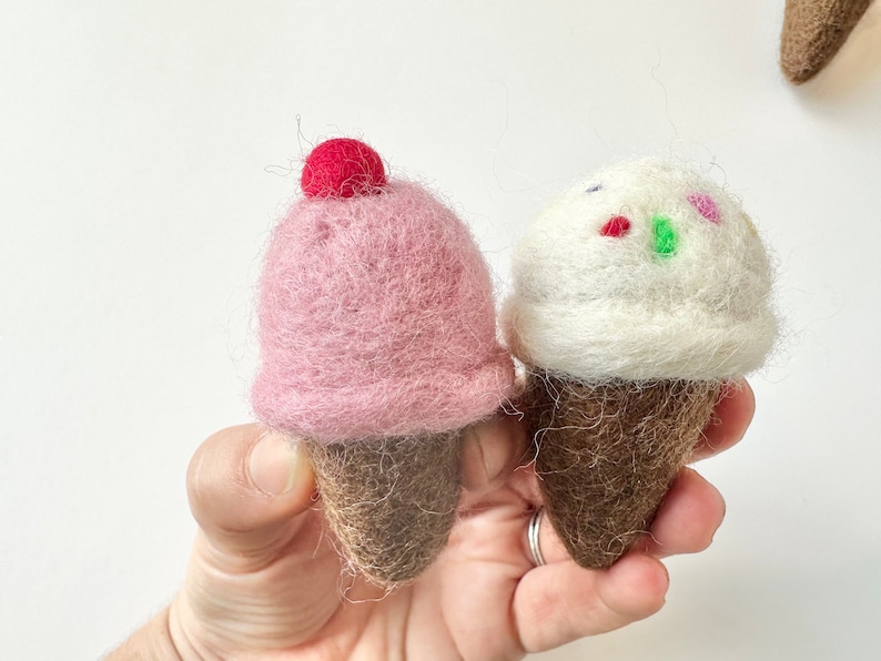Pode incluir: Dois cones de gelado de feltro. Um &eacute; rosa com uma cereja vermelha no topo. O outro &eacute; branco com granulado colorido. Ambos t&ecirc;m cones castanhos.