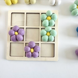 Pu&ograve; includere: Una griglia di legno con nove quadrati, ognuno contenente un fiore di feltro. I fiori sono di vari colori, tra cui viola, blu, verde e giallo.