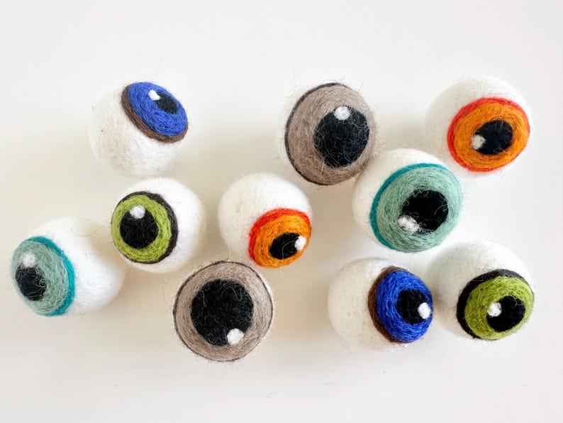 May include: Nine felt eyeballs with different colored irises and pupils. The eyeballs are white with a black outline and are all different colors, including blue, green, orange, and brown.