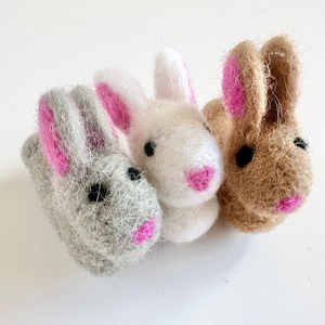 May include: Three felt bunny finger puppets. One is gray, one is white, and one is brown. Each bunny has pink ears and a pink nose.