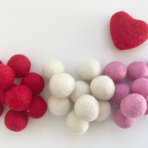 May include: A collection of felt balls in red, white, and pink colors. There is also a red felt heart.